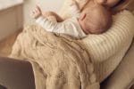 Mama trzyma na kolanach niemowlę okryte kocykiem bambusowym Ivi w kolorze cappuccino