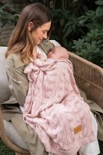 Mother holding a sleeping baby covered with the Ivi bamboo blanket in dusty pink
