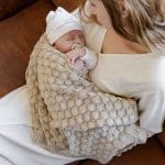 Newborn with a pacifier wrapped in the beige Fema bamboo blanket, held by his mother