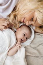 Mama leży obok niemowlęcia otulonego kremową pieluszką muślinową