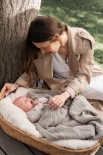 Mother sitting by a basket with a baby covered by the cappuccino Bono merino blanket