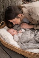 Mother kissing a baby lying in a basket under the Bono merino blanket in cappuccino
