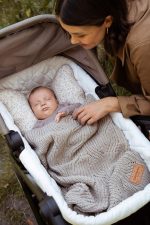 Mother looking into a pram where a baby sleeps under the openwork Bono merino blanket