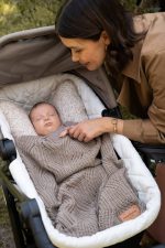 Baby asleep in a pram bassinet covered with the dark beige Bono merino blanket