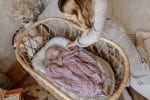 Mother over a baby in a Moses basket covered with the Fema bamboo blanket in misty rose