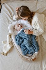 Baby in the Happy Goose baby nest covered with an ocean blue blanket, mother beside