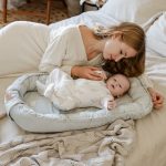 Mama czule dotyka niemowlęcia w kokonie Happy Goose Olive na łóżku