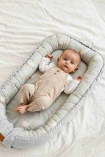 Baby in beige dungarees lying in the olive Happy Goose Olive baby nest