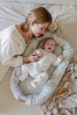 Roześmiane niemowlę w kokonie Happy Goose Olive, nad nim pochylona mama
