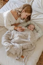 Mama nad niemowlęciem w kokonie Happy Goose Olive przykrytym beżowym kocykiem bambusowym Ivi