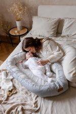 Mother cuddling a baby in a sleepsuit lying in the Happy Goose Olive baby nest