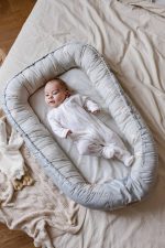 Baby lying in the olive Happy Goose Olive baby nest laid out on a bed, top view