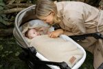 Mama pochyla się nad wózkiem z niemowlęciem otulonym otulaczem Baranek w kolorze ciepły beż