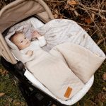 Baby in a pram on the Birdsong swaddle with a quilted beige outer layer