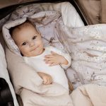 Smiling baby lying on the opened Birdsong swaddle with bird print