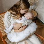 Mama całuje niemowlę leżące na poduszce do karmienia Happy Goose w gąski