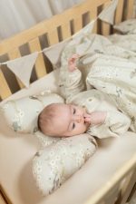 Niemowlę na poduszce motylek Birdsong w łóżeczku, obok zmięta kołdra w ptaszki