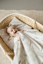 Laughing baby in a Moses basket on a Birdsong pillow, covered with a duvet