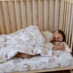 Laughing boy lying in a cot under the Forest Friends duvet with a woodland animal print