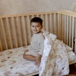 Boy sitting in a cot with the Forest Friends duvet draped over his shoulders