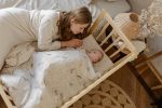 Mother lying by the cot looking at a baby covered with Birdsong bedding