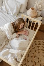 Mama gładzi główkę niemowlęcia śpiącego na poduszce Herbs w łóżeczku