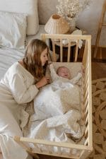 Mama czuwa przy łóżeczku z niemowlęciem otulonym pościelą Herbs w gałązki