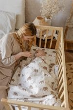 Mother tucking in a baby sleeping in a wooden cot under the Temo bear print bedding