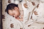 Newborn sleeping with a hand by its face on the Temo pillow with brown bears