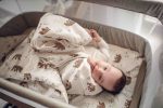 Niemowlę leżące w łóżeczku turystycznym na poduszce Temo, przykryte kołderką w misie