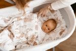 Mother tucking a baby in a bassinet under the Forest Friends duvet with fawns