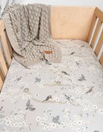 Birdsong fitted sheet in a wooden cot with a beige textured knit blanket