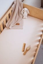 Warm beige fitted sheet in a cot with a blanket, bunny toy and brush