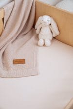 Close-up of a warm beige fitted sheet with a blanket and a plush bunny