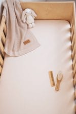 Cot with a plain warm beige fitted sheet and a bunny toy