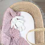 White fitted sheet in a Moses basket with a dusty pink blanket and plush bunny