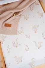 Zbliżenie na nadruk gąsek i kłosów na prześcieradle Happy Goose, obok beżowy kocyk