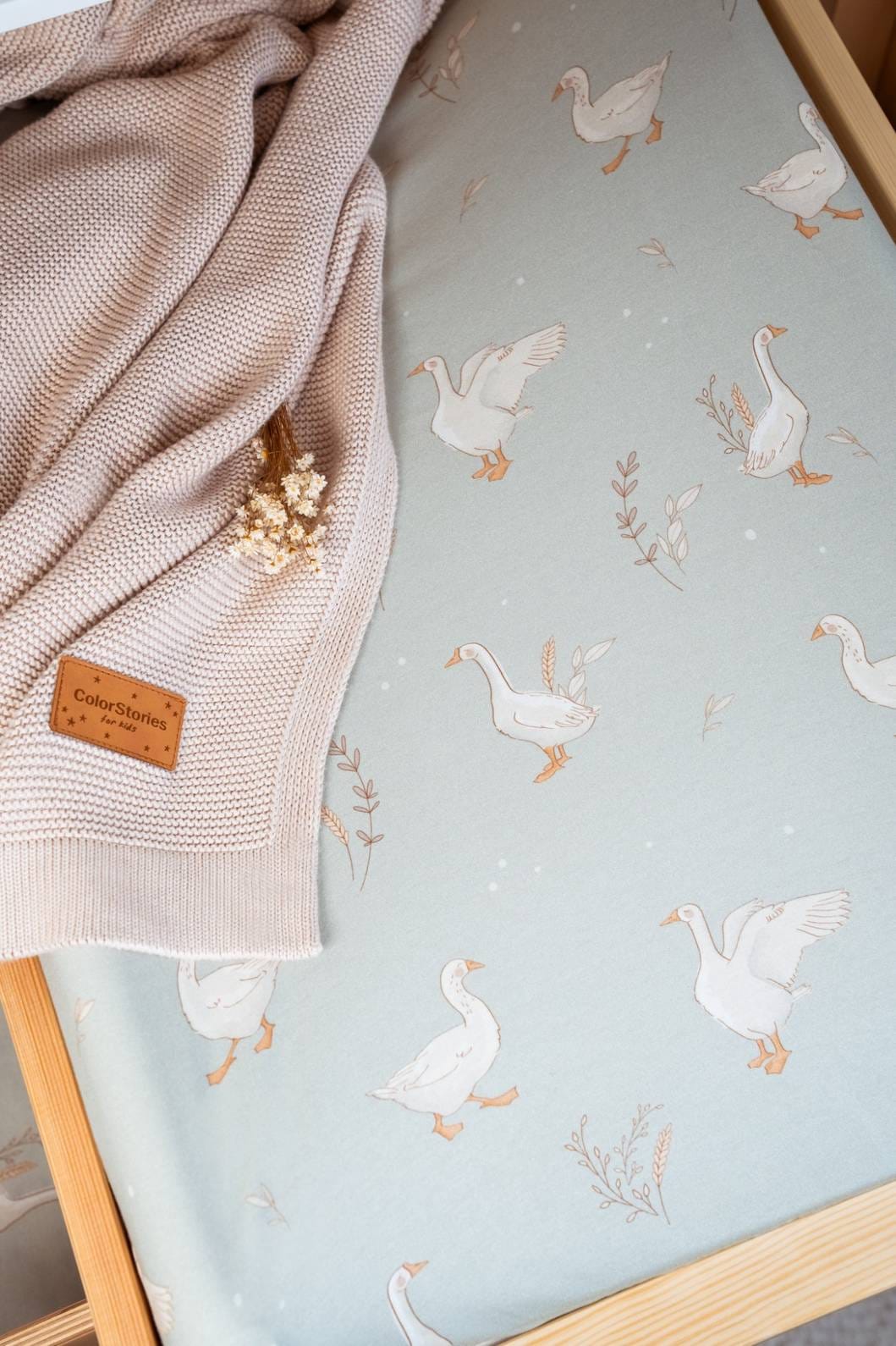 Close-up of white geese on the sage Happy Goose Olive cover, with a beige blanket
