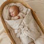 Baby in the Birdsong swaddle wrap tied with a bow, lying in a wicker basket