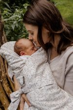 Mother cuddling a newborn wrapped in the Herbs swaddle wrap with a tiny herb print in a garden