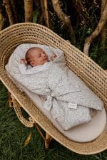 Newborn in the Herbs swaddle wrap tied with a bow in a wicker basket on the grass
