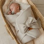 Sleeping newborn with a dummy in the beige muslin swaddle wrap with a large bow in a basket