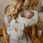 Mother holding a newborn in the beige muslin swaddle wrap tied with a bow