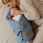 Mama całuje niemowlę zawinięte w niebieski rożek muślinowy