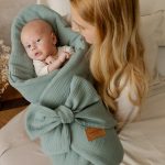 Mama trzyma niemowlę w oliwkowym rożku muślinowym ze skórzaną metką