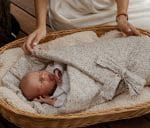 Mother settling a newborn in the tie-up Herbs swaddle wrap in a wicker basket