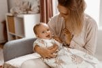 Smiling baby in the Forest Friends sleeping bag sitting with mother on a sofa