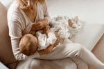 Mother feeding a baby in the Forest Friends sleeping bag while sitting on a sofa