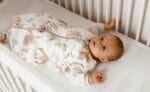 Baby in the Forest Friends sleeping bag lying in a white cot