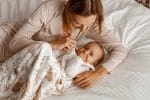 Mother playing with the hands of a baby in the Forest Friends sleeping bag on a bed